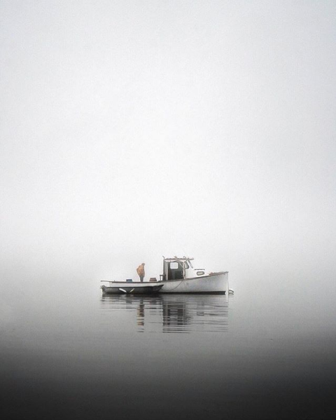 A lobster boat sits in calm waters and dense fog