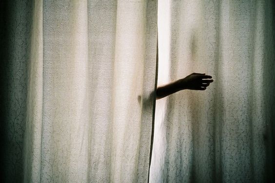 A seemingly disembodied arm reaches out from between two curtains
